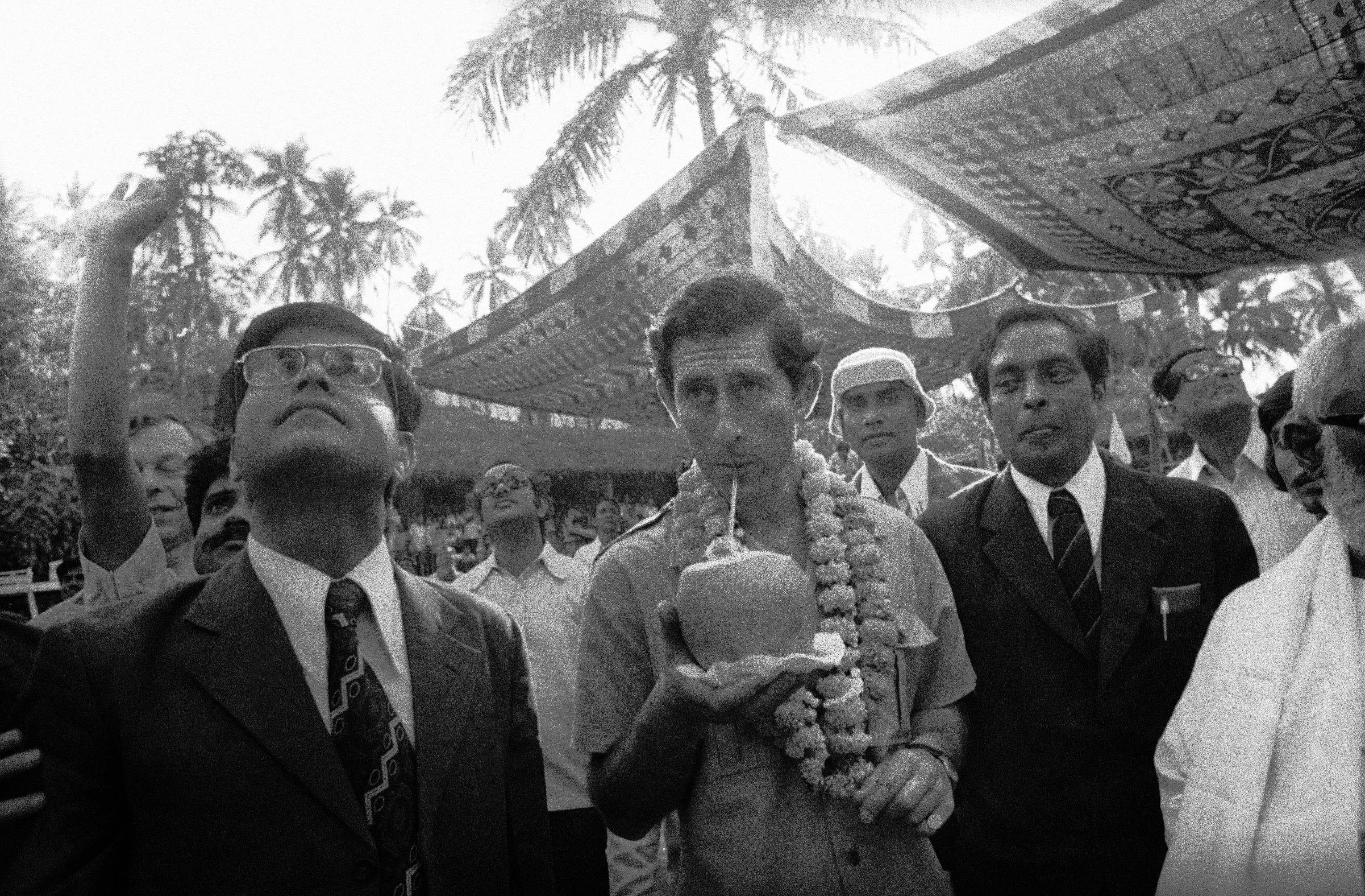 FILE - In this Dec. 4, 1980 file photo, Britain's Prince Charles, centre, drinks juice from a freshly-cut green coconut at Haripur village which he visited during a one-day halt in Bhubaneswar, India. Prince Charles has been preparing for the crown his entire life. Now, that moment has finally arrived. Charles, the oldest person to ever assume the British throne, became king on Thursday Sept. 8, 2022, following the death of his mother, Queen Elizabeth II. (AP Photo/Santosh Basak, File)