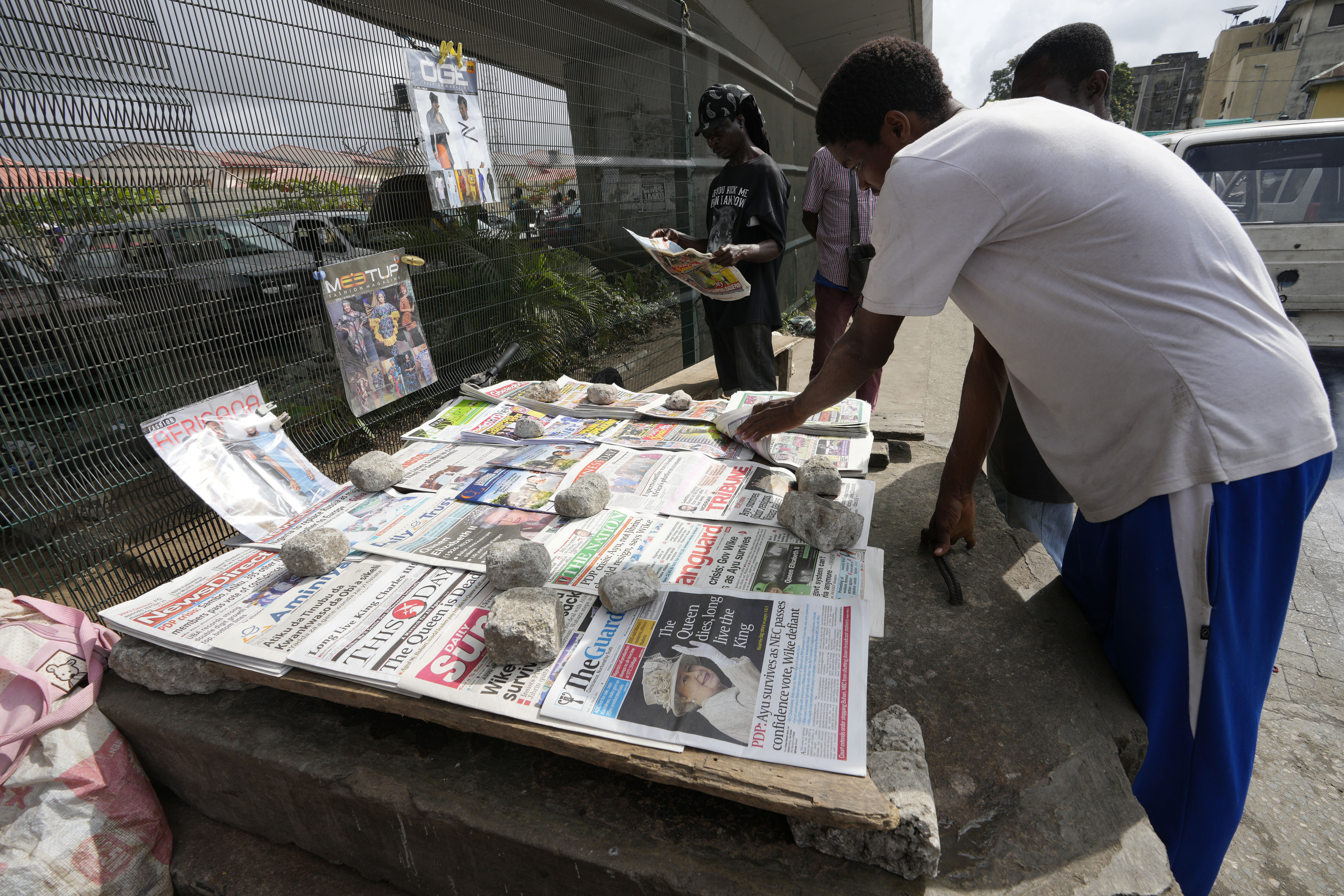 People reads newspapers with a front page photo of Britain's Queen Elizabeth II at a newsstand in Obalende Lagos, Nigeria Friday , Sept. 9, 2022. Queen Elizabeth II, Britain's longest-reigning monarch and a rock of stability across much of a turbulent century, died Thursday Sept. 8, 2022, after 70 years on the throne. She was 96. (AP Photo/ Sunday Alamba)