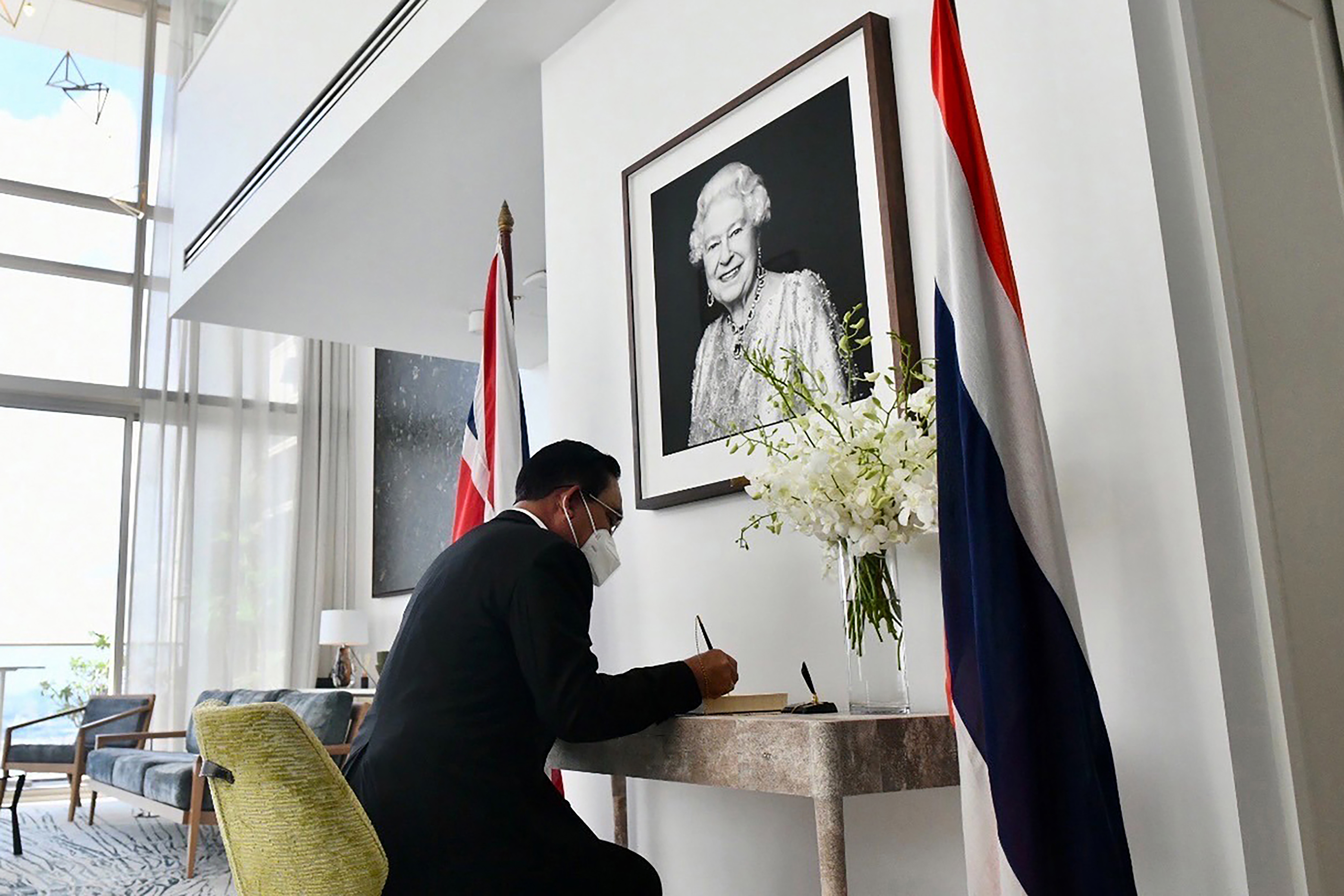 In this photo release by Government Spokesman Office, Thailand Defense Minister Prayuth Chan-ocha, currently suspended as Thailand's prime minister while a court decides a legal challenge against him, signs a book of condolence in front of a picture of Queen Elizabeth II at British Ambassador's Residence in Bangkok, Thailand, Friday, Sept. 9, 2022. Queen Elizabeth II, Britain's longest-reigning monarch and a rock of stability across much of a turbulent century, died Thursday Sept. 8, 2022, after 70 years on the throne. She was 96. (Thailand Government Spokesman Office via AP)