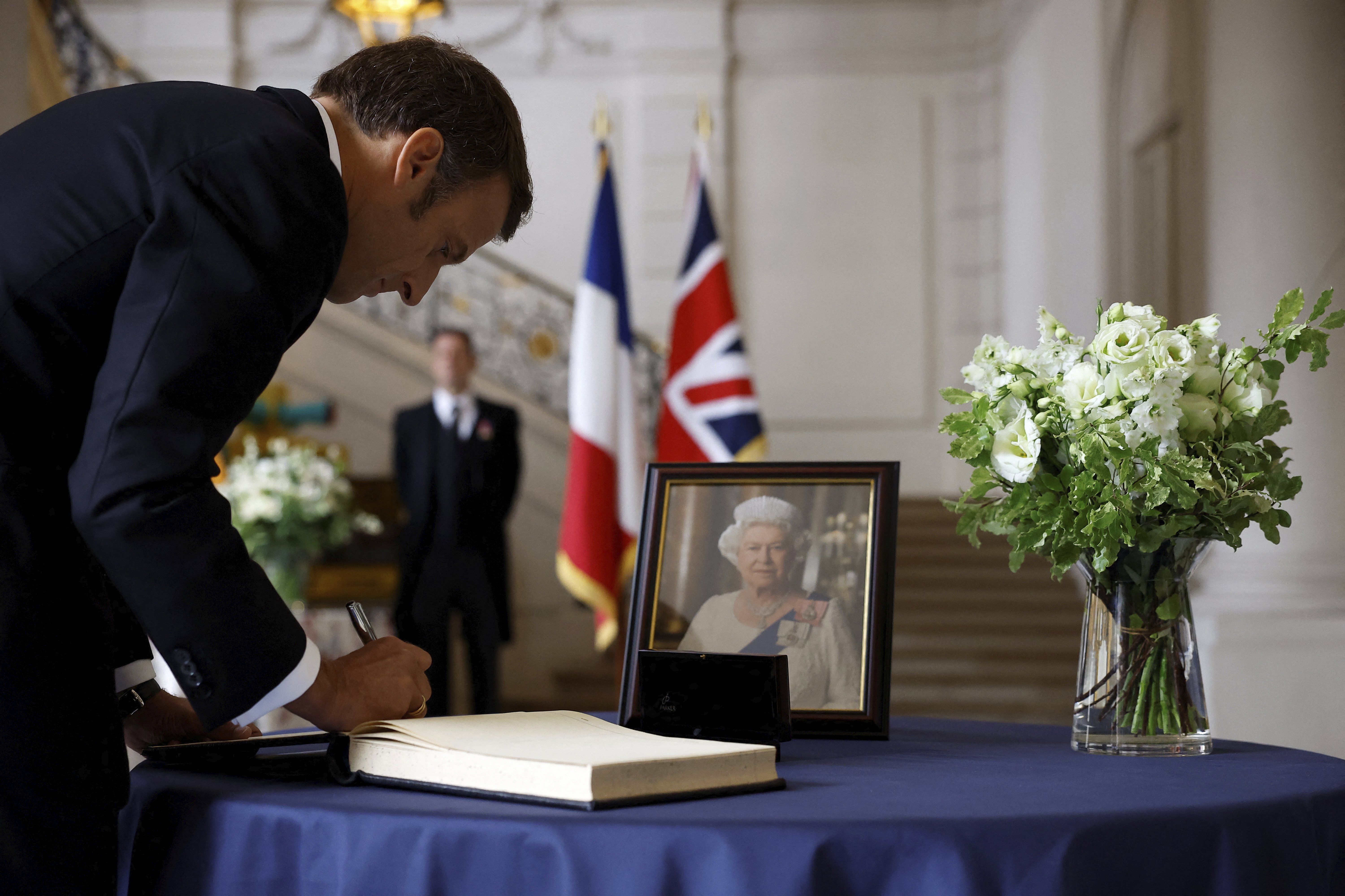 French President Emmanuel Macron signs a condolence book, following the passing of Britain's Queen Elizabeth, at the British Embassy in Paris, France, Friday, Sept. 9, 2022. Britain's longest-reigning monarch and a rock of stability across much of a turbulent century, died Thursday after 70 years on the throne. She was 96. (Christian Hartmann/Pool via AP)