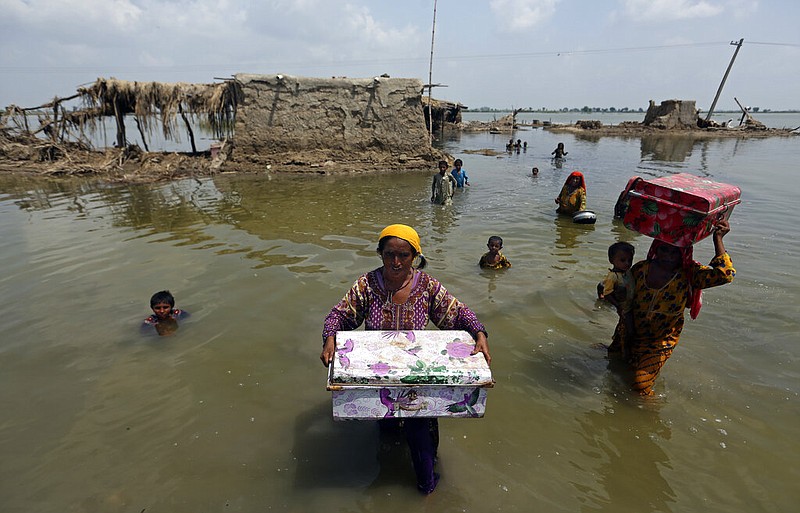 FILE - Women carry belongings salvaged from their flooded home after monsoon rains, in the Qambar Shahdadkot district of Sindh Province, of Pakistan, Sept. 6, 2022. From drought to floods and sea level rise, the cost of damage caused by climate change will only get higher as the world warms, sparking concerns from both top officials and activists about how to pay for it. (AP Photo/Fareed Khan, File)