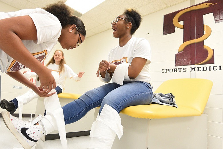 Staff photo by Matt Hamilton / Ayoni Hardy, left, 16, uses toilet paper to simulate bandaging the leg of Katreya Lewis, 16, at Tyner Academy on Wednesday, September 14, 2022.