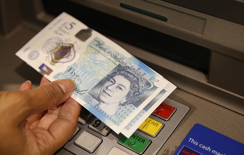 In this Sept. 13, 2016 file photo, a member of staff at a branch of Halifax bank, in London, displays a new British 5 pound sterling note, made from polymer. (AP Photo/Alastair Grant, File)