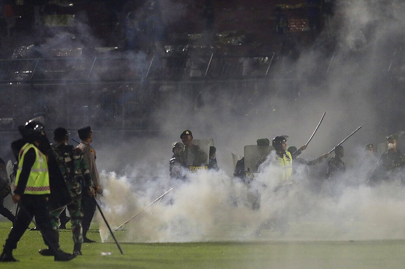 Police officers and soldiers stand amid tear gas smoke after clashes between fans during a soccer match at Kanjuruhan Stadium in Malang, East Java, Indonesia, Saturday, Oct. 1, 2022. (AP/Yudha Prabowo)