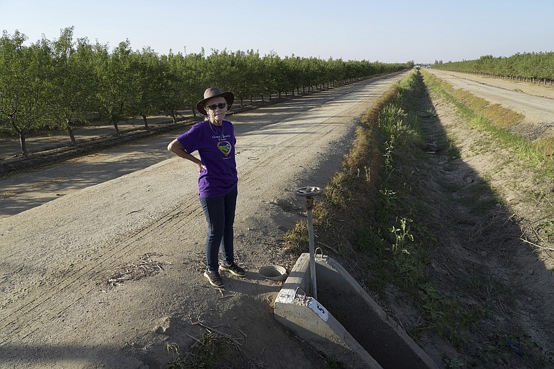 Elaine Moore stands next to a dry irrigation canal and almond orchard near her property, where two wells have gone dry this summer in Chowchilla, Calif., Sept. 14, 2022. (AP Photo/Terry Chea)