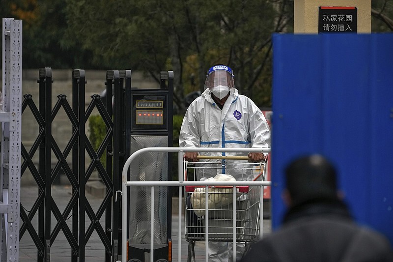 A worker in protective clothing transfers foods to a barricaded neighborhood locked down for health monitoring following a covid-19 case detected in the area Wednesday in Beijing.
(AP/Andy Wong)