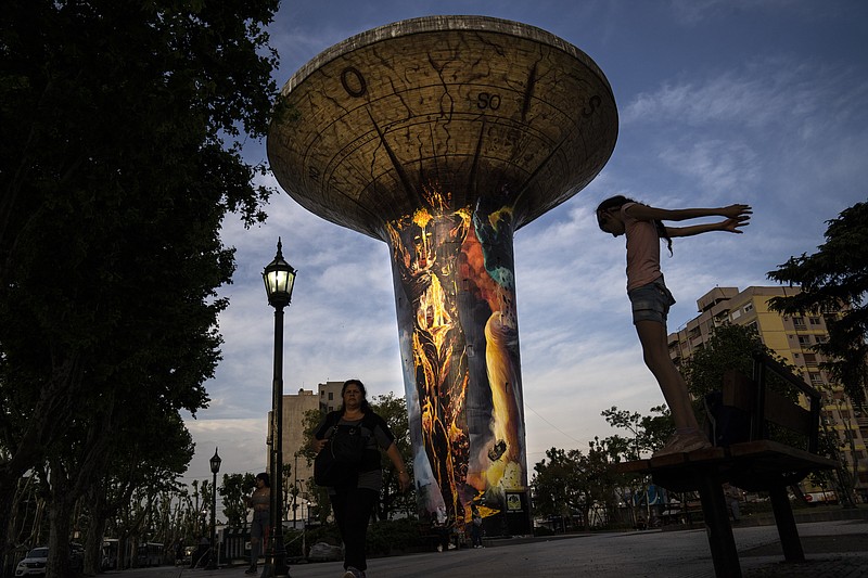 A water tank towers over the town's public square in Monte Grande, Argentina, Friday, Oct. 28, 2022. The enormous water tank became a work of art in 2020 when, at the municipality's request, artist Leandro García Pimentel painted a mural on it depicting fire, earth, air and water. (AP Photo/Rodrigo Abd)
