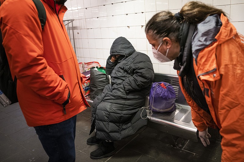 FILE - Homeless Outreach personnel reach out to a person sleeping on a bench in the Manhattan subway system, Monday, Feb. 21, 2022, in New York. In New York City's latest effort to address a mental health crisis on its streets and subways, Mayor Eric Adams announced Tuesday, Nov. 29, that authorities would more aggressively intervene to help people in need of treatment, saying there was "a moral obligation" to do so, even if it means providing care to those who don't ask for it. (AP Photo/John Minchillo, File)