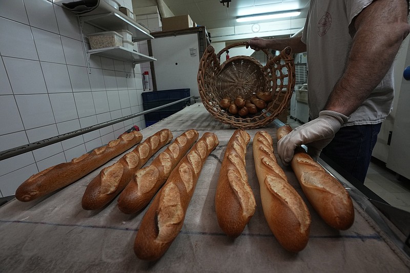 Baker David Buelens puts the baguettes into a basket at a bakery, in Versailles, west of Paris, Tuesday, Nov. 29, 2022. (AP Photo/Michel Euler)