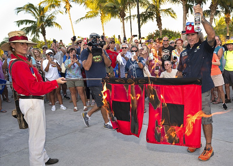 Jai Somers (left) holds hurricane flags that were doused with rum and set on fire by Paul Menta (right) to mark the end of the 2022 Atlantic hurricane season Wednesday in Key West, Fla.
(AP/Florida Keys News Bureau/Andy Newman)