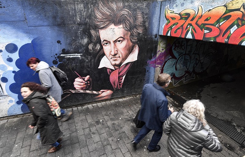 People passing a graffiti showing composer Ludwig van Beethoven on a street in Bonn, Germany, Wednesday, Feb. 19, 2020. The city of Bonn, where Beethoven was born on December 17, 1770, celebrated the 250th birthday of the great German composer with many cultural events.(AP Photo/Martin Meissner)