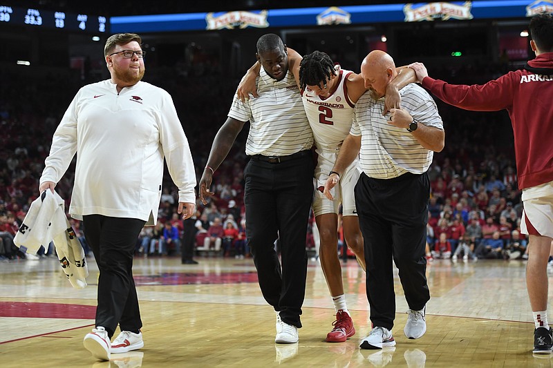 Arkansas forward Trevon Brazile (2) is helped off of the court Tuesday, Dec. 6, 2022, by recruiting coordinator Ronnie Brewer and strength coach Dave Richardson (right), as trainer Matt Townsend leads the way after Brazile injured his leg during the first half of play in Bud Walton Arena in Fayetteville.