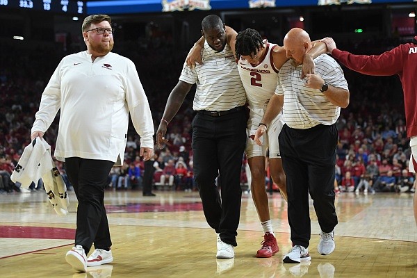 Arkansas forward Trevon Brazile (2) is helps off of the court Tuesday, Dec. 6, 2022, by recruiting coordinator Ronnie Brewer and strength coach Dave Richardson (right) as trainer Matt Townsend leads the way after injuring his leg during the first half of play in Bud Walton Arena in Fayetteville. Visit nwaonline.com/photo for the photo gallery.