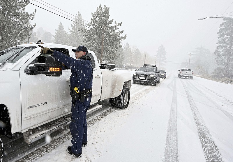 California Highway Patrol officer Mike Eshleman instructs a driver he may continue on Highway 2 in his 4-wheel drive vehicle as heavy snow falls near Wrightwood, Calif., on Monday, Dec. 12, 2022. (Will Lester/The Orange County Register via AP)