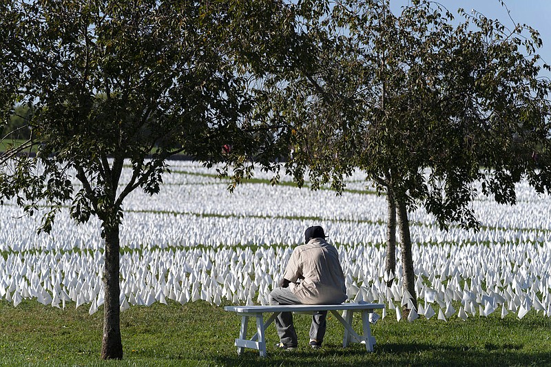 FILE - A visitor sits on a bench to look artist Suzanne Brennan Firstenberg's "In America: Remember," a temporary art installation made up of white flags to commemorate Americans who have died of COVID-19, on the National Mall in Washington on Oct. 2, 2021. The number of U.S. deaths has dropped in 2022 after soaring for two years during the COVID-19 pandemic, but it still is much higher than the levels before the coronavirus hit. (AP Photo/Jose Luis Magana, File)