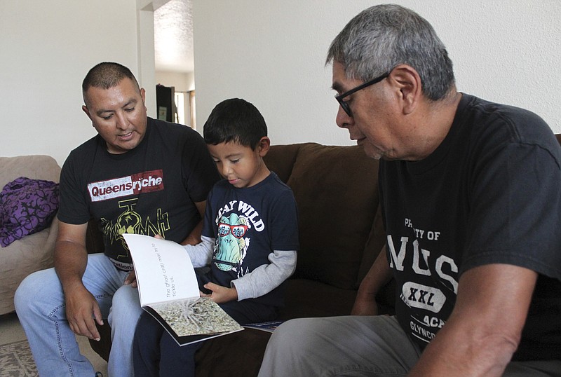 Micca Madalena, center, reads to his father, Darryl Madalena, left, and grandfather Myron Ami in his native language of Towa after getting home from school at Jemez Pueblo, N.M., Oct. 7, 2022. Darryl Madalena is advocating for more Native Americans to consider joining the organ donation rolls. (AP Photo/Susan Montoya Bryan)