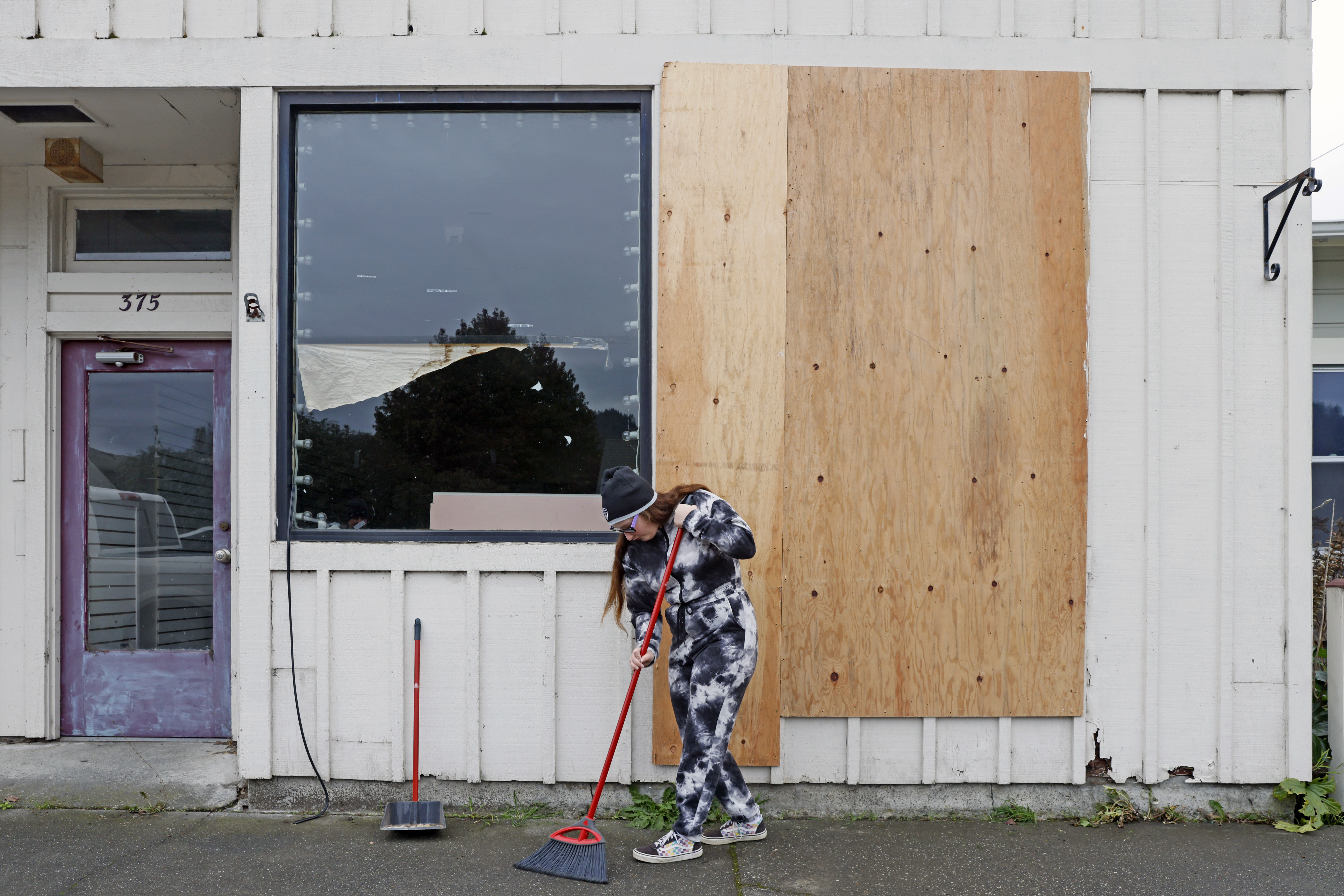 A person, who identified themselves as Michelle, sweeps the street from broken glass following an earthquake in Rio Dell, Calif., Tuesday, Dec. 20, 2022. (Santiago Mejia /San Francisco Chronicle via AP)