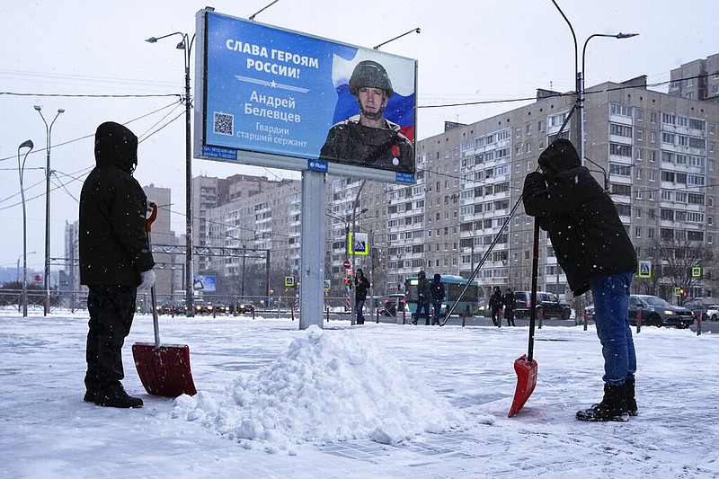 Workers clear the snow next to a billboard with a portrait of a Russian soldier awarded for action in Ukraine and the words "Glory to the heroes of Russia" in St. Petersburg, Russia, Tuesday, Jan. 3, 2023. (AP/Dmitri Lovetsky)
