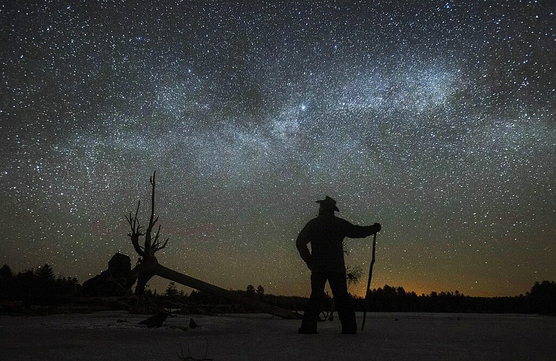 FILE - Dave Cooke observes the Milky Way over a frozen fish sanctuary in central Ontario, north of Highway 36 in Kawartha Lakes, Ontario, Canada, early Sunday, March 21, 2021. According to research published in the journal Science on Thursday, Jan. 19, 2023, every year the night sky grows brighter, and the stars look dimmer. Analyzing data from more than 50,000 citizen scientists, or amateur stargazers, reveals that artificial lighting is making the night sky about 10% brighter each year, a faster rate of change that scientists had previously estimated looking at satellite data. (Fred Thornhill/The Canadian Press via AP)