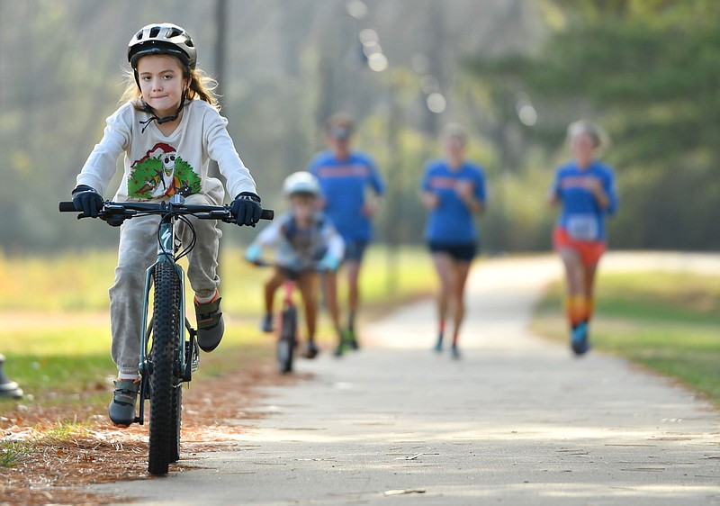 Audrey Denham (from left), 8, leads the way as Reece Denham, 6; Kevin Cox; Crystal Cox; and Charity Cox ride and run together on a trail in Gulley Park in Fayetteville in this Nov. 25, 2022 file photo. (NWA Democrat-Gazette/Andy Shupe)