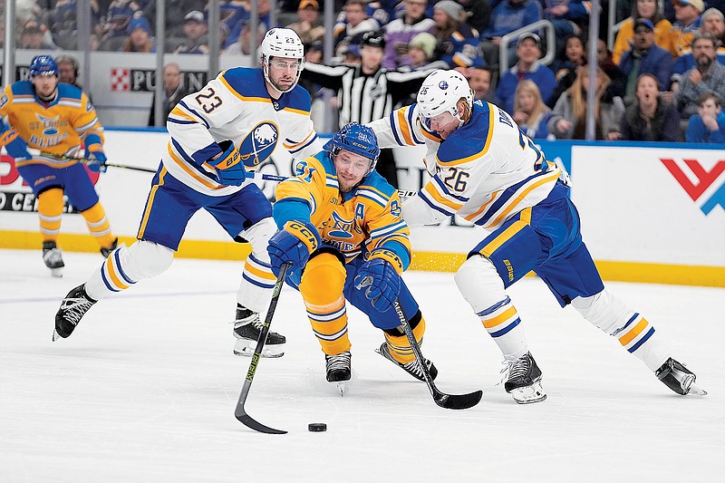 Vladimir Tarasenko of the Blues reaches for a loose puck as Sabres' teammates Rasmus Dahlin (26) and Mattias Samuelsson (23) defend during the second period of Tuesday night's game at Enterprise Center in St. Louis. (Associated Press)