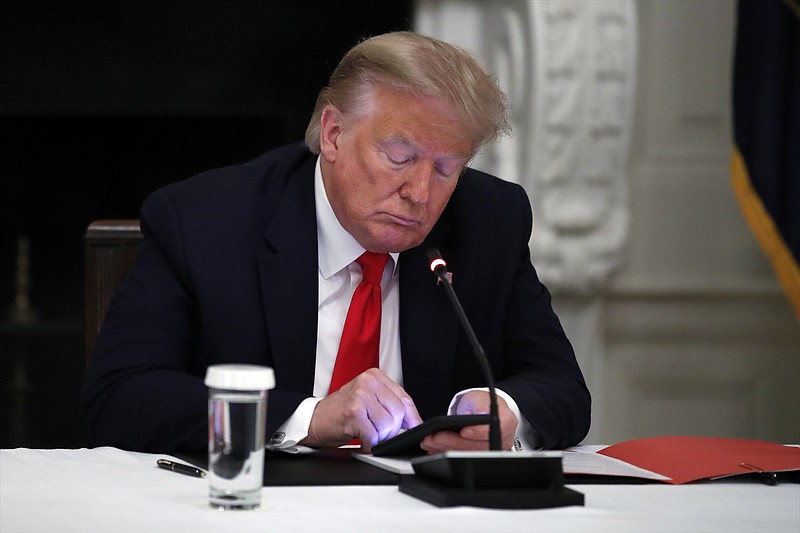 FILE - In this Thursday, June 18, 2020 file photo, President Donald Trump looks at his phone during a roundtable with governors on the reopening of America's small businesses, in the State Dining Room of the White House in Washington. (AP Photo/Alex Brandon, File)