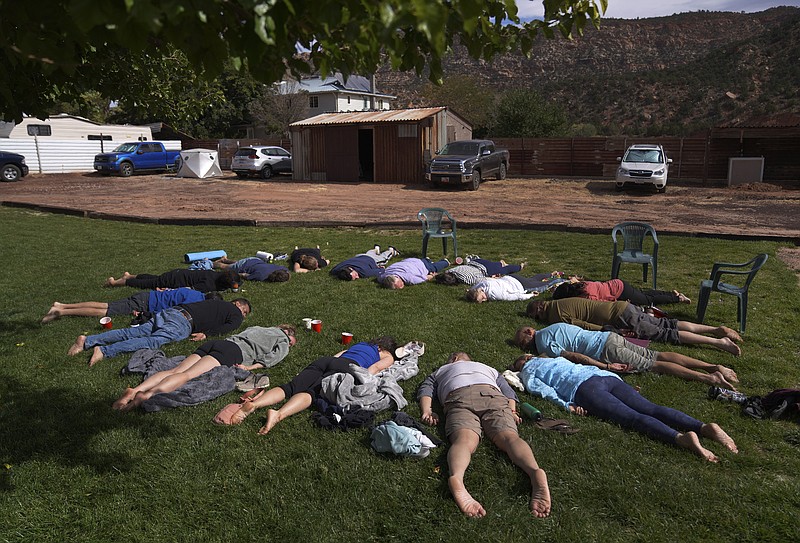 Participants lay face down on the grass during an integration circle at an ayahuasca retreat in Hildale, Utah, on Saturday, Oct. 15, 2022. Following each of the three ayahuasca ceremonies, Hummingbird Church asks their participants to partake in integration, or a group reflection and discussion, to help interpret messages they received from the ayahuasca. (AP Photo/Jessie Wardarski)