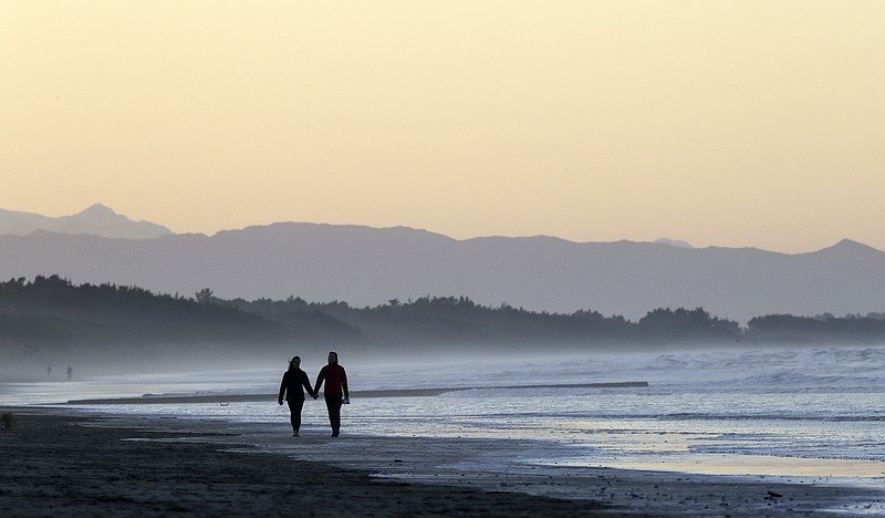FILE - A couple walk along New Brighton Beach at sunset in Christchurch, New Zealand, Tuesday, June 9, 2020. (AP Photo/Mark Baker, File)