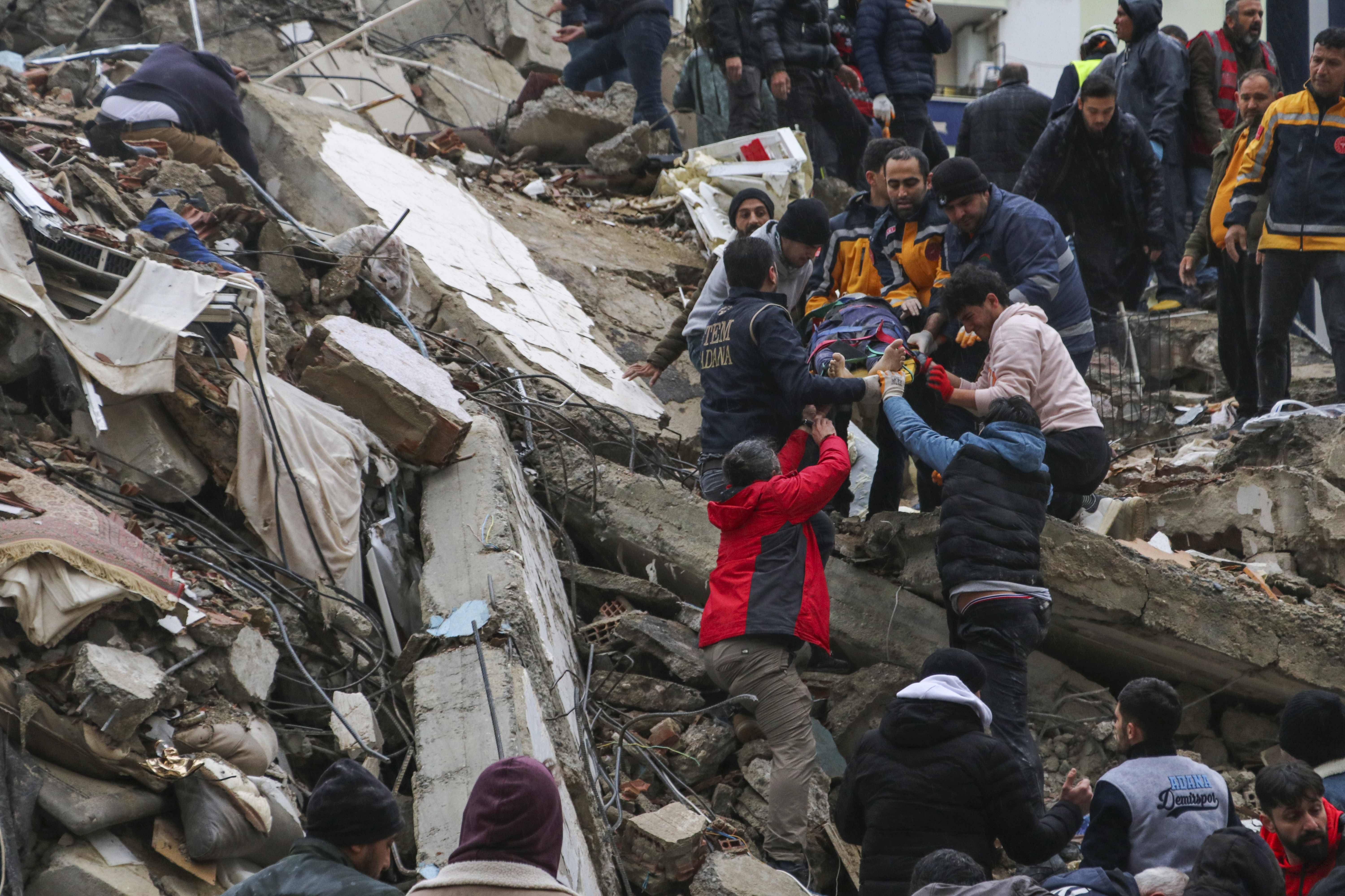 People and emergency teams rescue a person on a stretcher from a collapsed building in Adana, Turkey, Monday, Feb. 6, 2023. A powerful quake has knocked down multiple buildings in southeast Turkey and Syria and many casualties are feared. (IHA agency via AP)