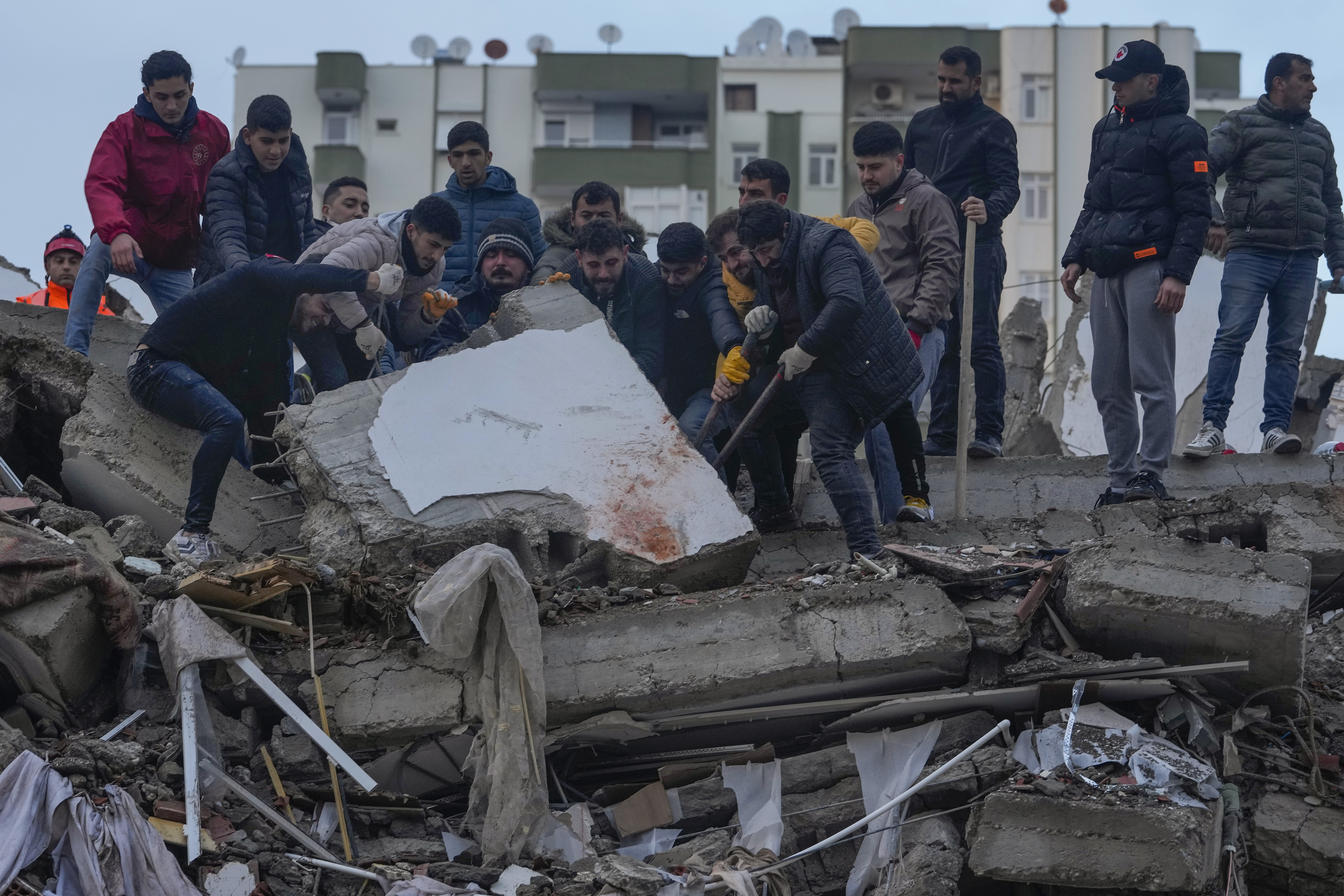 Men search for people among the debris in a destroyed building in Adana, Turkey, Monday, Feb. 6, 2023. A powerful quake has knocked down multiple buildings in southeast Turkey and Syria and many casualties are feared. (AP Photo/Khalil Hamra)