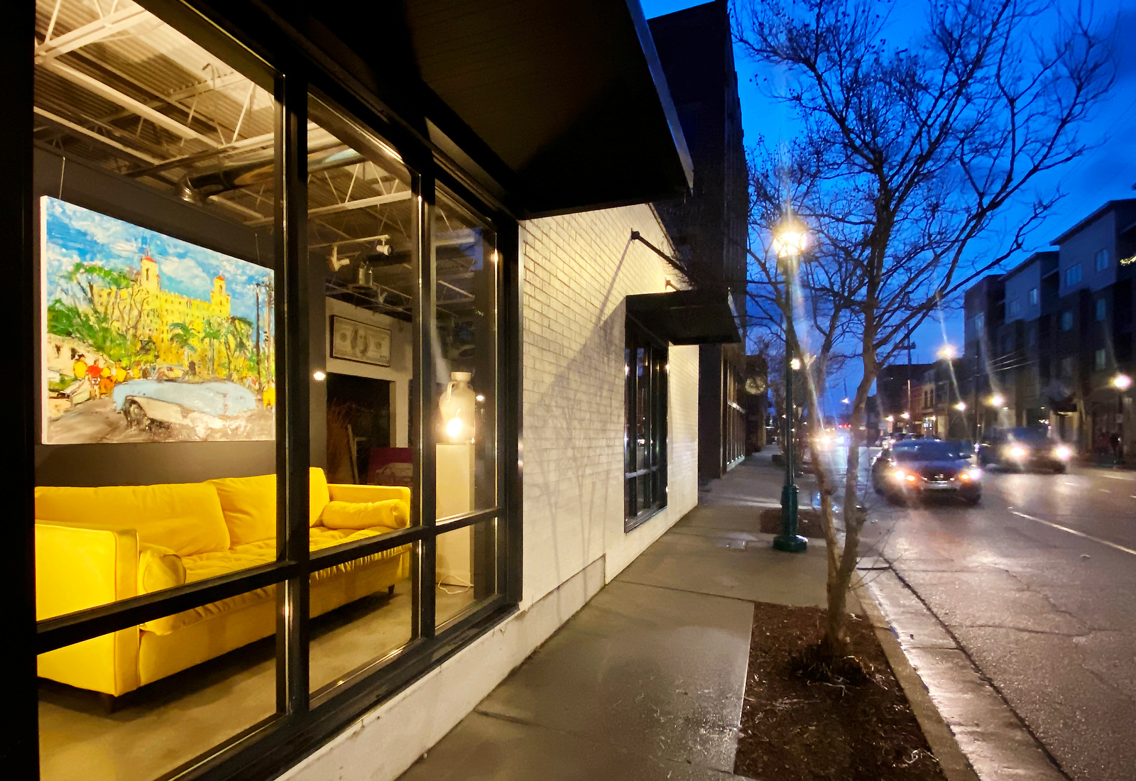 Staff Photo by Robin Rudd / The warmth of window at Gallery 1401 contrasts with the blue dawn along Main Street on February 21, 2023.  Above the yellow couch hands artist Ana Guzman's 