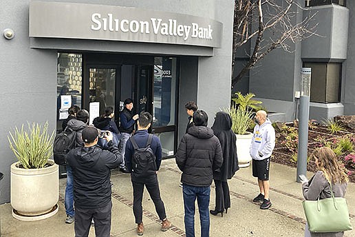 An employee stands at the door of Silicon Valley Bank in Santa Clara, Calif., on Friday as people wait outside. Federal regulators shut the bank down as depositors scrambled to withdraw funds.
(AP/Jeff Chiu)