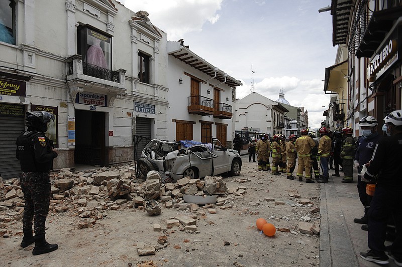 Rescue workers stand next to a car crushed by debris after an earthquake in Cuenca, Ecuador, Saturday, March 18, 2023. (AP/Xavier Caivinagua)