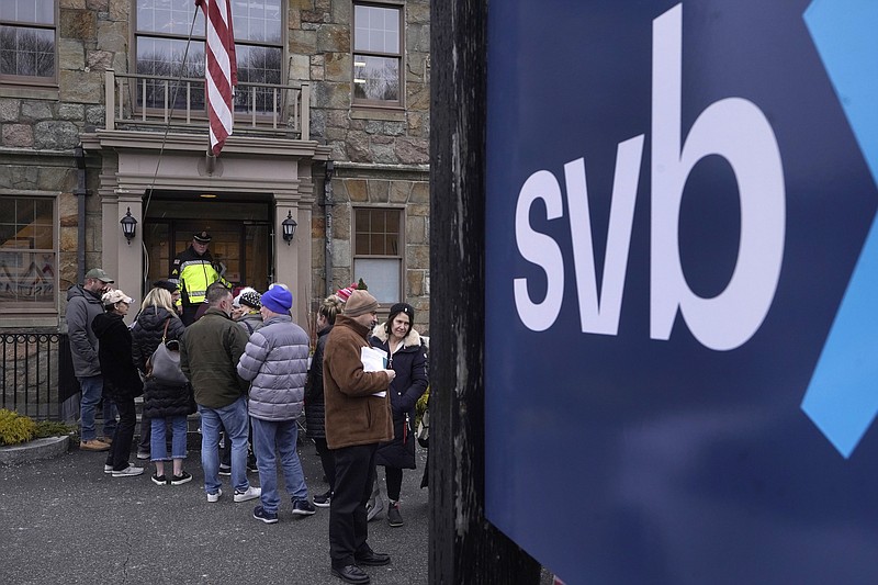 FILE - A law enforcement official, behind, stands in an entryway to a Silicon Valley Bank branch location, March 13, 2023, as customers and bystanders line up outside the bank, in Wellesley, Mass. A new poll finds that only 10% of U.S. adults say they have high confidence in the nation’s banks and other financial institutions. That's down from the 22% who said they had high confidence in banks in 2020. Following the collapse of Silicon Valley Bank this month, the poll from The Associated Press-NORC Center for Public Affairs Research also finds that a majority say the government is not doing enough to regulate the industry. (AP Photo/Steven Senne, File)