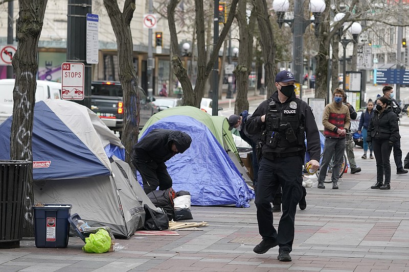 FILE - A Seattle police officer walks past tents used by people experiencing homelessness, March 11, 2022, during the clearing and removal of an encampment in Westlake Park in downtown Seattle. (AP Photo/Ted S. Warren, File)
