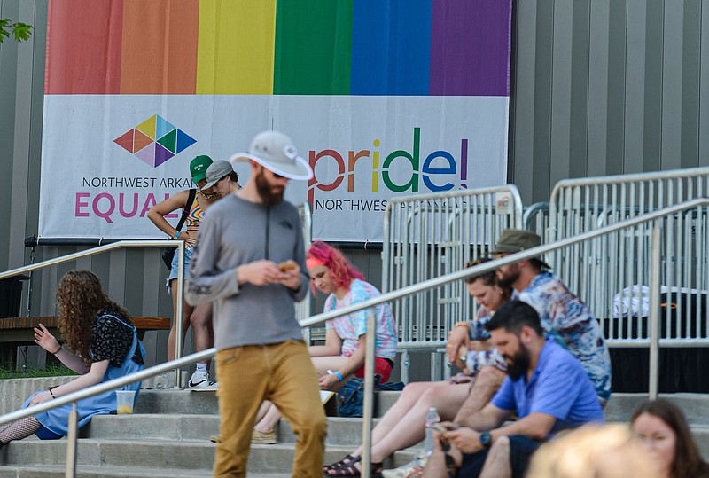 Attendees rest in the shade next to a Pride flag outside the Walton Arts Center in Fayetteville during the 2022 Northwest Arkansas Pride Weekend in this June 18, 2022 file photo. (NWA Democrat-Gazette/Hank Layton)