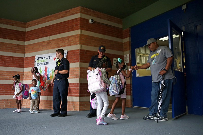 Derek Witcher (far right) greets students at the entrance to Gibbs Magnet Elementary School in Little Rock on the first day of class in this Aug. 22, 2022 file photo. Witcher joined other members of the Little Rock Fire Department to welcome the students to the school in the Little Rock School District. (Arkansas Democrat-Gazette/Colin Murphey)