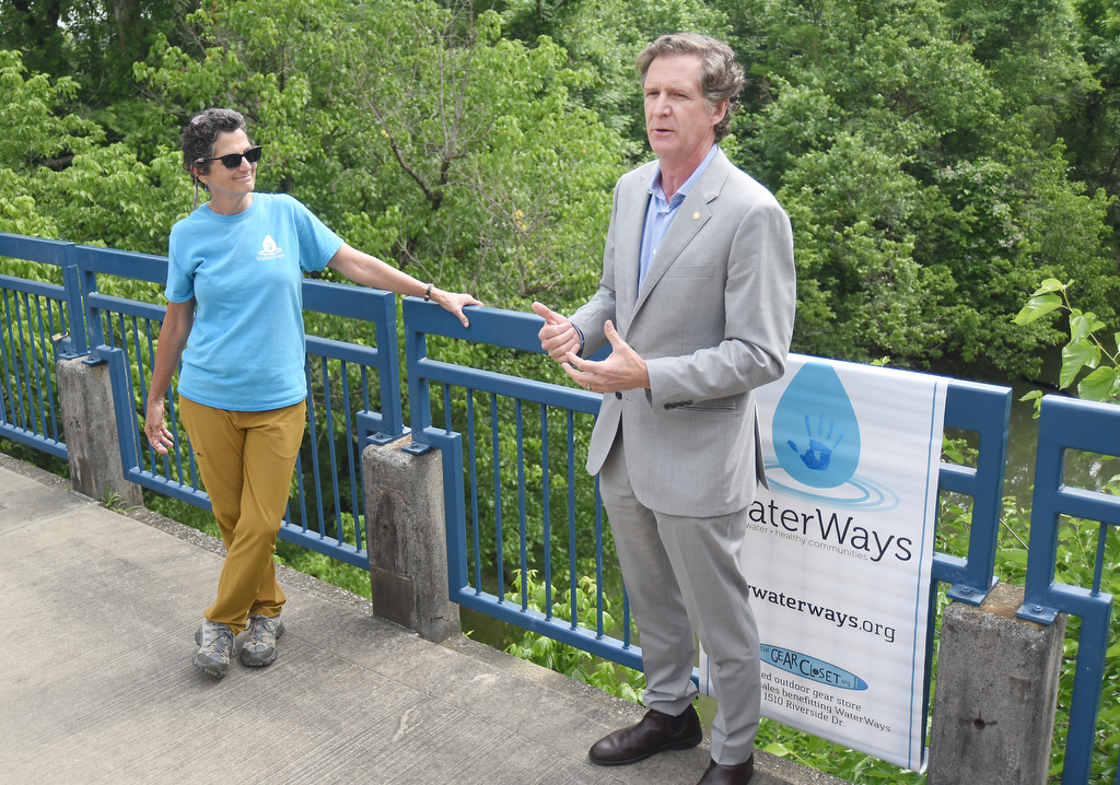 Staff photo by Matt Hamilton / WaterWays executive director Mary Beth Sutton, left, looks on as Mayor Tim Kelly speaks on the Tennessee River Walk about the trash booms on Tuesday, May 23, 2023.
