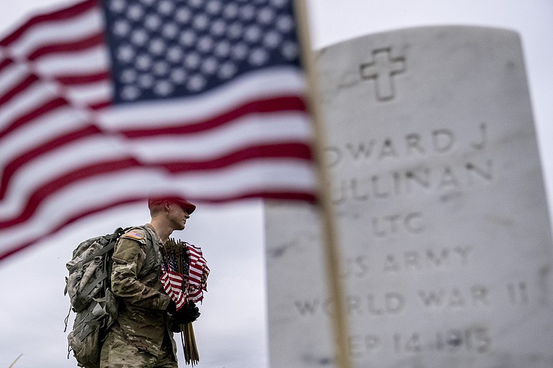 A member of the 3rd U.S. Infantry Regiment, also known as The Old Guard, places flags in front of each headstone for "Flags-In" at Arlington National Cemetery in Arlington, Thursday, May 25, 2023, to honor the Nation's fallen military heroes ahead of Memorial Day. (AP Photo/Andrew Harnik)