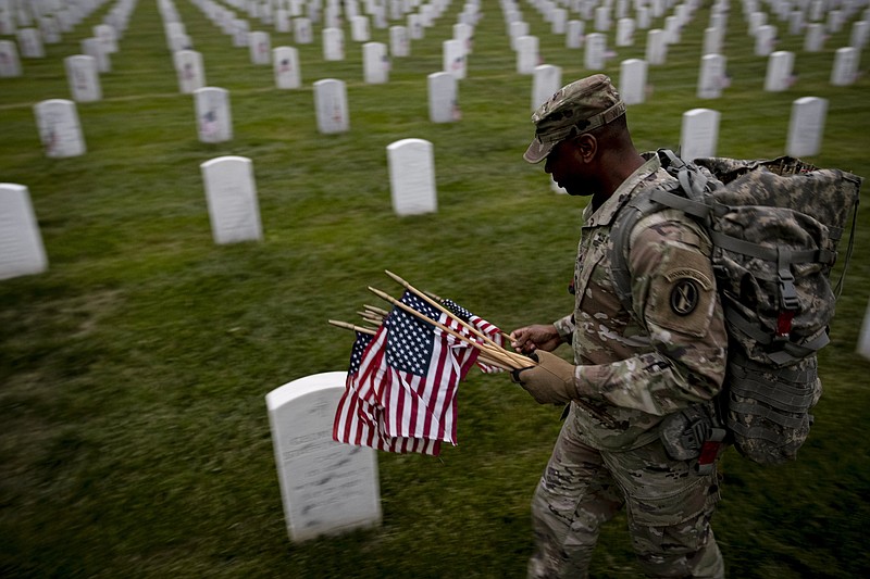 A member of the 3rd U.S. Infantry Regiment also known as The Old Guard, places flags in front of each headstone for "Flags-In" before sunrise at Arlington National Cemetery in Arlington, Thursday, May 25, 2023, to honor the Nation's fallen military heroes ahead of Memorial Day. (AP Photo/Andrew Harnik)