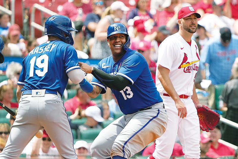 Salvador Perez is helped up by Royals teammate Michael Massey after scoring a run as Cardinals starting pitcher Adam Wainwright walks behind during the fifth inning of Monday afternoon’s game at Busch Stadium in St. Louis. (Associated Press)