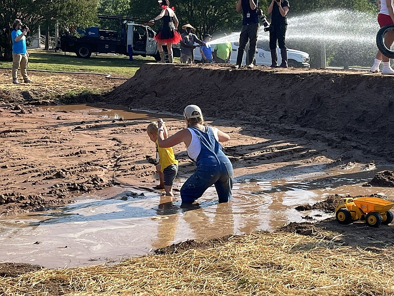 A volunteer helps a child through the mud pit at Little Rock’s annual Mud Run on Saturday, June 3, 2023 at War Memorial Park. (Arkansas Democrat-Gazette/Jason Batacao)
