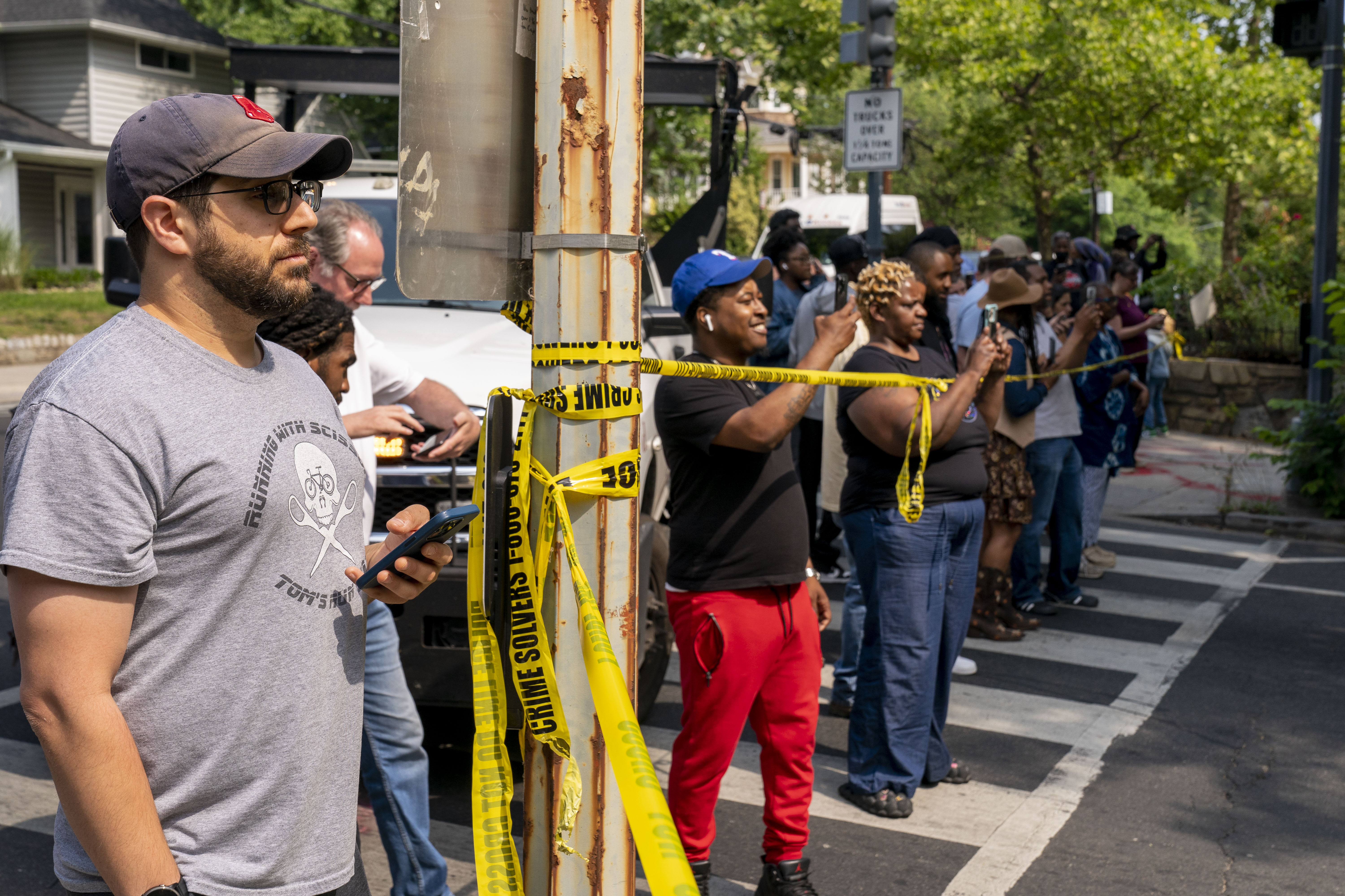 Residents stand at police tape to try to get a view of a black bear in the residential Brookland neighborhood in Northeast Washington, in Washington, Friday, June 9, 2023. The bear was eventually tranquilized by the Humane Rescue Alliance and taken away in a cage by the Smithsonian's National Zoo. (AP Photo/Andrew Harnik)