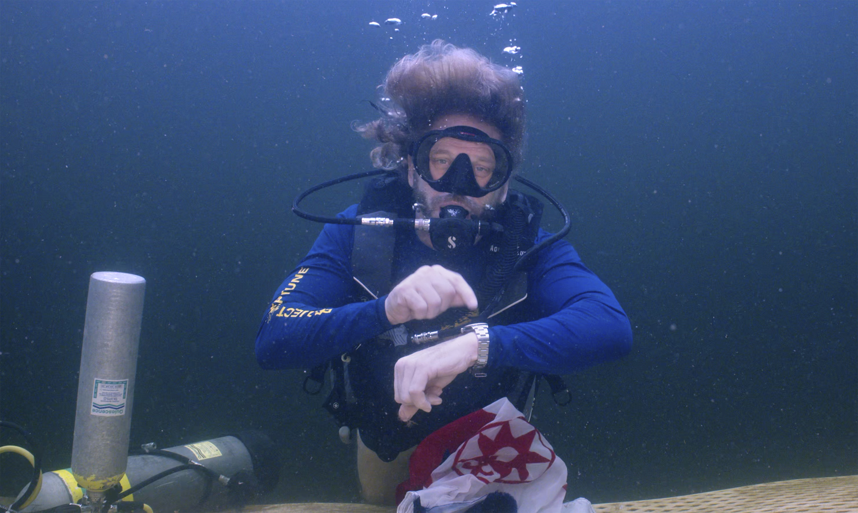 In this photo provided by the Florida Keys News Bureau, diving explorer and medical researcher Dr. Joseph Dituri points to his watch Friday, June 9, 2023, indicating that it is time to surface after spending 100 days in the Jules' Undersea Lodge marine habitat at the bottom of a Key Largo, Fla., lagoon. Dituri broke the previous 73-day record for underwater human habitation at ambient pressure, undertook medical and marine science research and interacted online with more than 5,500 students during his Project Neptune 100 mission organized by the Marine Resources Development Foundation. (Mariano Lorde/Florida Keys News Bureau via AP)