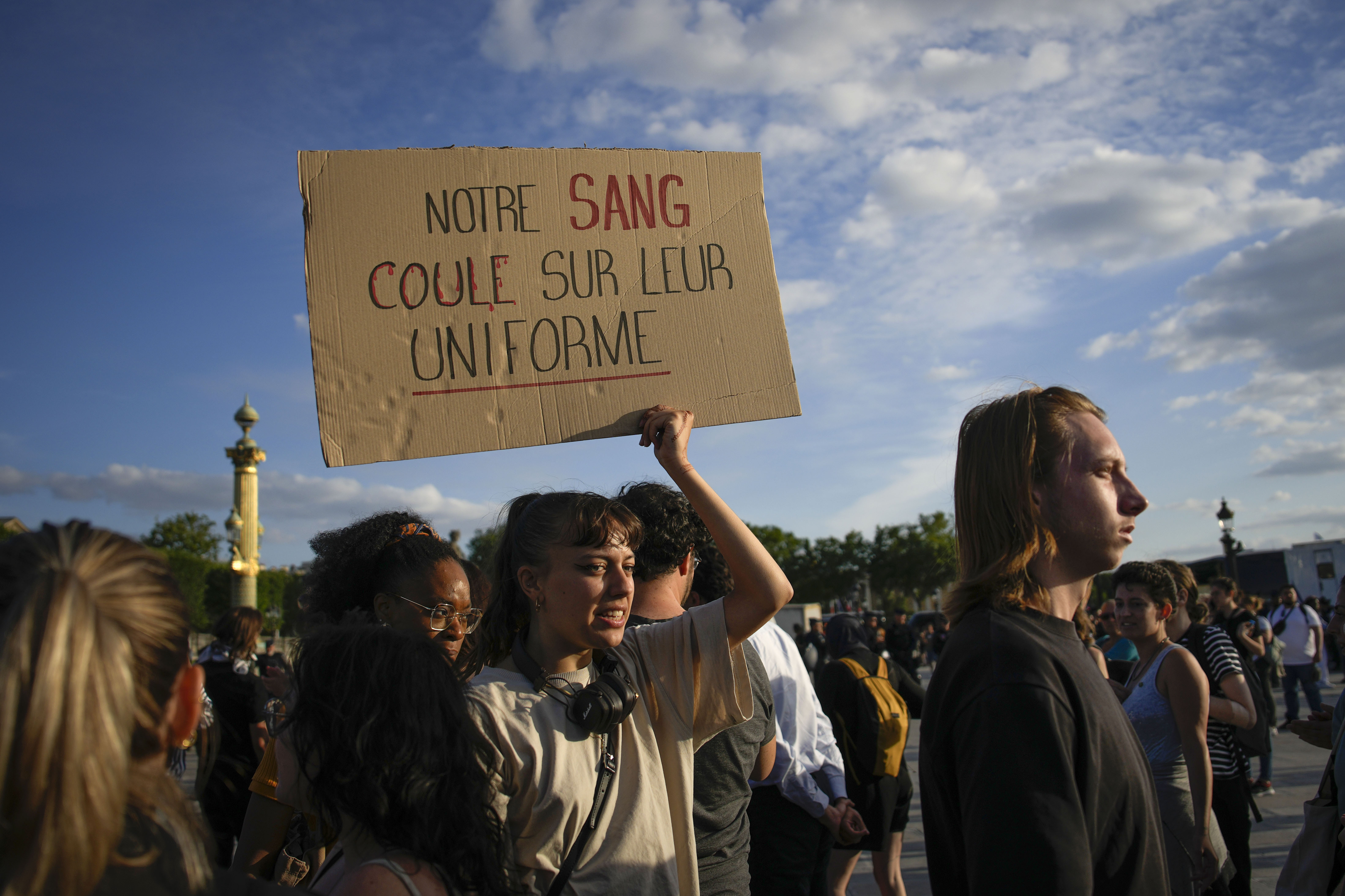 A woman holds a placard reading "Our blood runs on their uniform" during a protest in Paris, France, Friday, June 30, 2023. French President Emmanuel Macron urged parents Friday to keep teenagers at home and proposed restrictions on social media to quell rioting spreading across France over the fatal police shooting of a 17-year-old driver. (AP Photo/Lewis Joly)