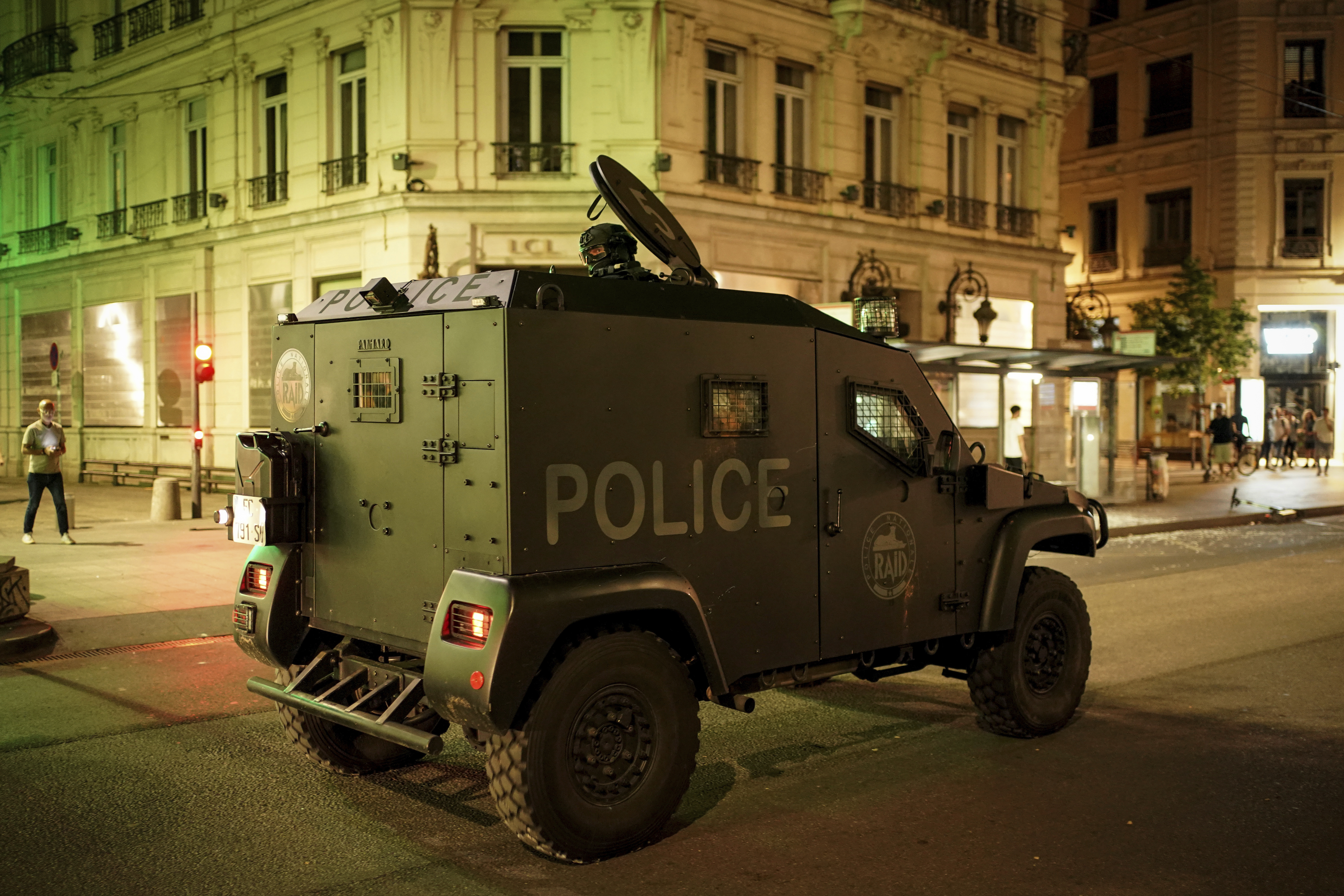 RAID police officers patrol during clashes in Lyon, central France, Friday, June 30, 2023. French President Emmanuel Macron urged parents Friday to keep teenagers at home and proposed restrictions on social media to quell rioting spreading across France over the fatal police shooting of a 17-year-old driver. Writing on wall reads in French "Justice for Nahel" (AP Photo/Laurent Cipriani)