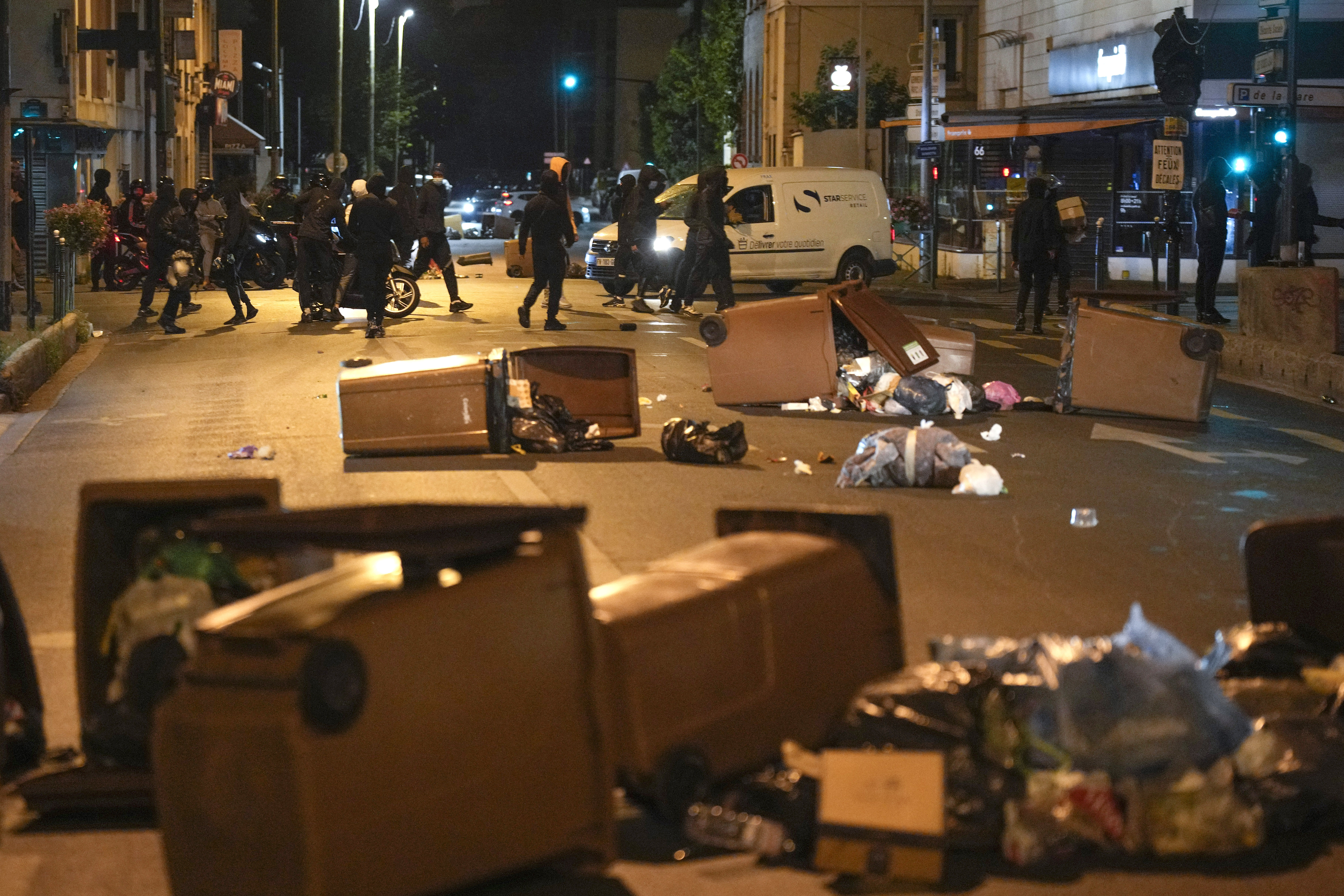 Protesters block a street with garbage cans in Colombes, outside Paris, France, Saturday, July 1, 2023. French President Emmanuel Macron urged parents Friday to keep teenagers at home and proposed restrictions on social media to quell rioting spreading across France over the fatal police shooting of a 17-year-old driver. (AP Photo/Lewis Joly)