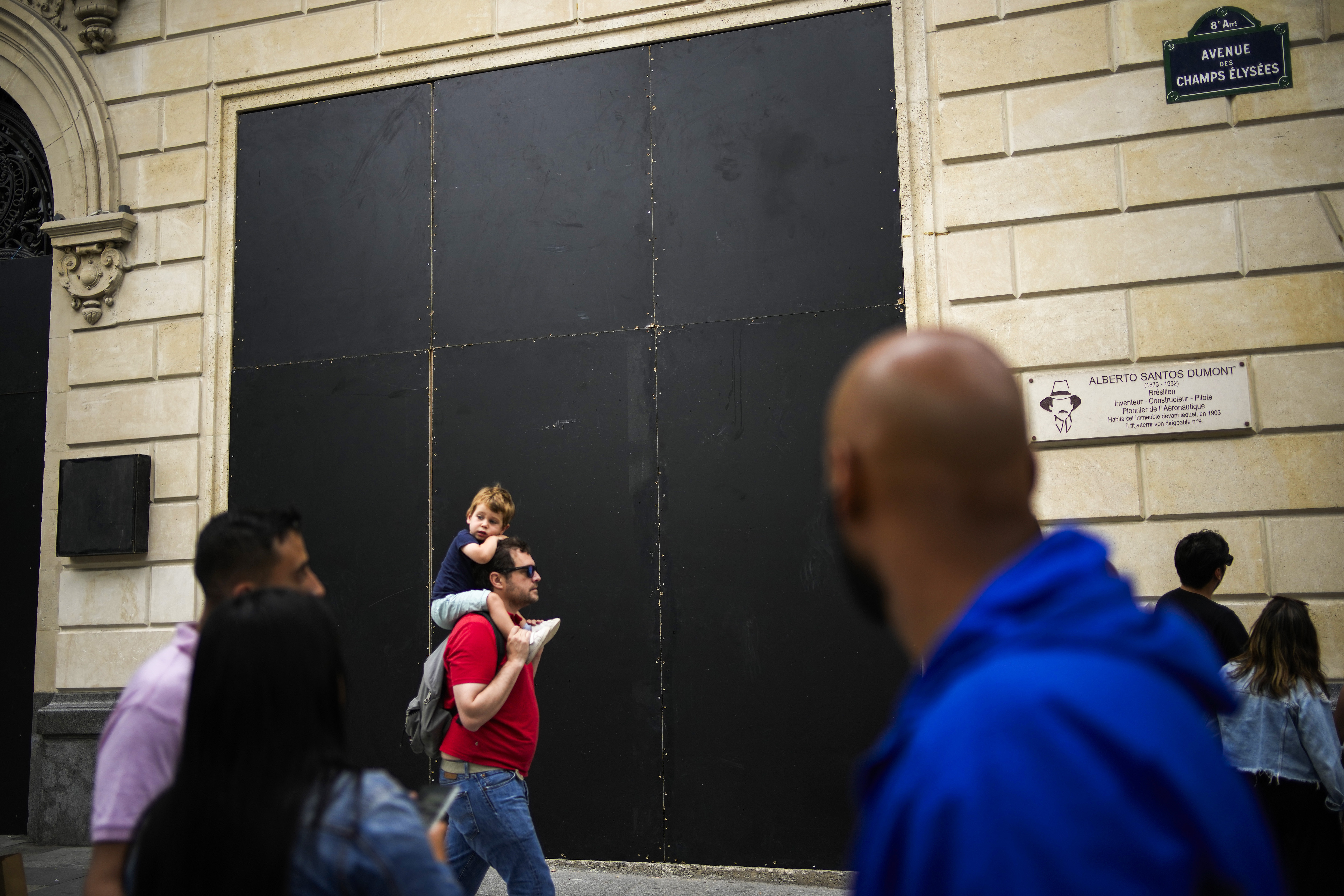 People walk past an Apple store covered with protection wood planks on the Champs-Elysees avenue in Paris, Saturday, July 1, 2023. The fatal shooting of Nahel, whose last name has not been made public, stirred up long-simmering tensions between police and young people in housing projects who struggle with poverty, unemployment and racial discrimination. (AP Photo/Christophe Ena)