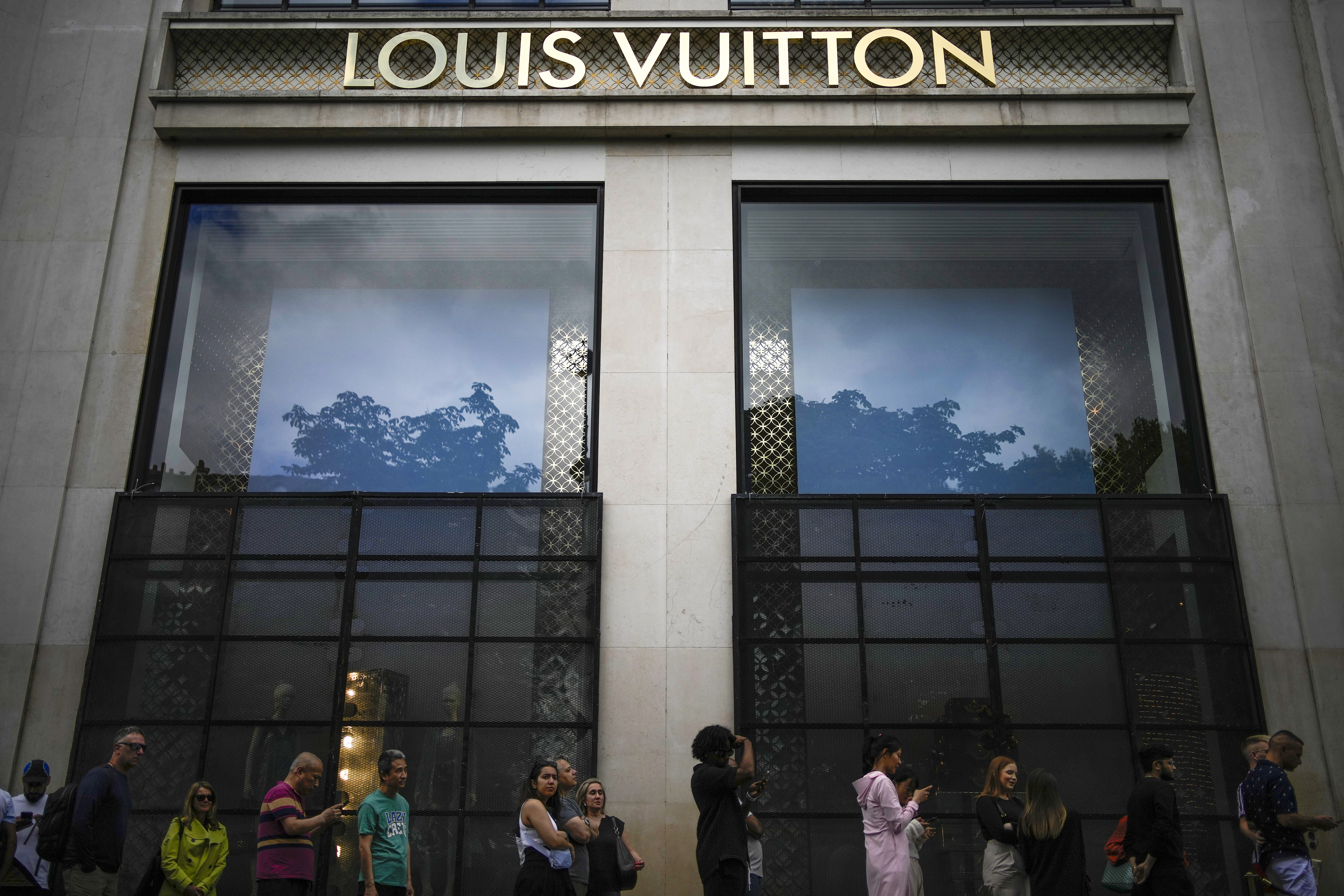 People wait in a queue outside a luxury shop blocked with security fences on the Champs-Elysees avenue in Paris, Saturday, July 1, 2023. The fatal shooting of Nahel, whose last name has not been made public, stirred up long-simmering tensions between police and young people in housing projects who struggle with poverty, unemployment and racial discrimination. (AP Photo/Christophe Ena)