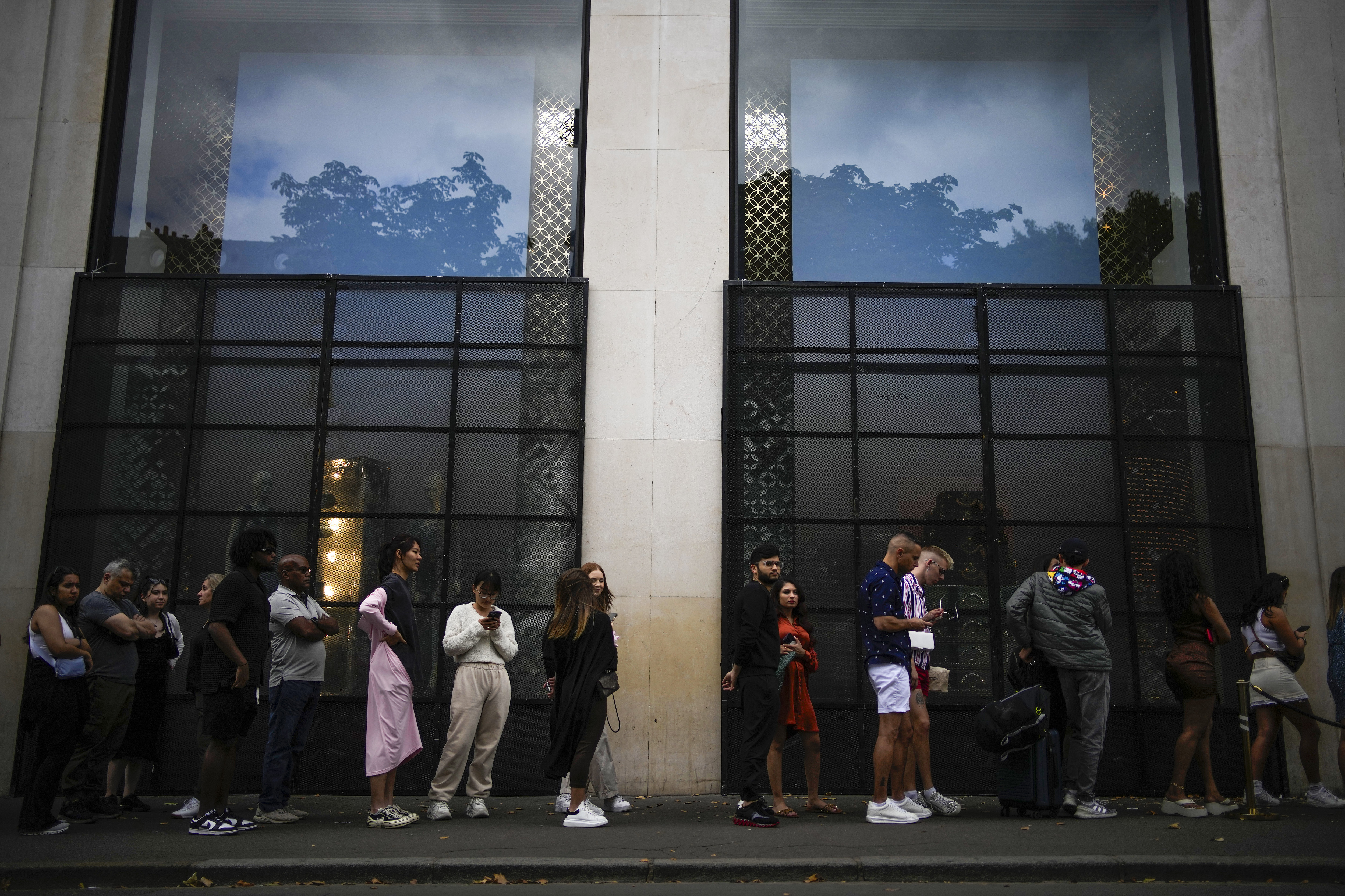 People wait in a queue outside a luxury shop blocked with security fences on the Champs-Elysees avenue in Paris, Saturday, July 1, 2023. The fatal shooting of Nahel, whose last name has not been made public, stirred up long-simmering tensions between police and young people in housing projects who struggle with poverty, unemployment and racial discrimination. (AP Photo/Christophe Ena)